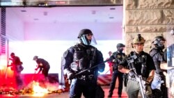 Law enforcement officers stand watch and extinguish a fire set by protesters behind the Mark O. Hatfield United States Courthouse, Aug. 2, 2020, in Portland.
