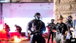 Law enforcement officers stand watch and extinguish a fire set by protesters behind the Mark O. Hatfield United States Courthouse, Aug. 2, 2020, in Portland.