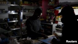 Un commerçant vend des articles sous la lumière d'une lampe à piles pendant une coupure d’électricité au Cap, Afrique du Sud, 15 avril 2015.