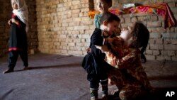 Fariha, a 13-month-old polio victim whose legs are bound in small plastic braces, is attended by her older sister Sana, Aziz Khan Ghari, Pakistan, May 30, 2012.