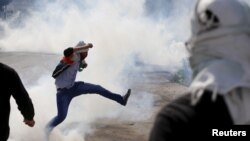 在西岸冲突中，一名巴勒斯坦抗议者踢走以色列军队投掷的催泪弹。（2015年10月29日）