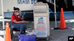 A poll worker wears personal protective equipment as she monitors a ballot drop box for mail-in ballots outside of a polling station during early voting, in Miami Beach, Florida. Aug. 7, 2020.