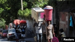 FILE - People carry their belongings along a street as they flee their homes from gang violence, in Port-au-Prince, Haiti, Oct. 26, 2024.
