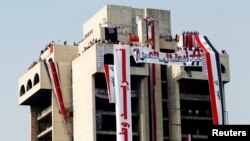 Demonstrators are seen on a building with Iraqi flags during a protest over corruption, lack of jobs, and poor services, in Baghdad, Oct. 29, 2019. 