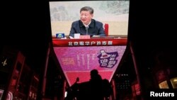 Seorang pria mengendarai skuter melewati layar raksasa yang menayangkan cuplikan berita Presiden China Xi Jinping yang menghadiri pertemuan politbiro Partai Komunis China, di Beijing, China, 9 Desember 2024. (Tingshu Wang/REUTERS)