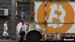 FILE - People walk past a board with the logo of Bitcoin in a street in Yerevan, Armenia September 9, 2019. (REUTERS/Anton Vaganov)