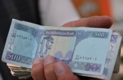 A money changer holds Afghan afghani bills along a street in Kabul on June 30, 2021.