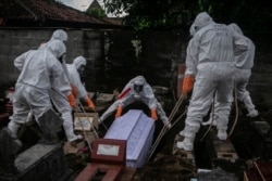 Para pegawai dinas pemakaman dengan mengenakan alat pelindung diri (APD) sedang memakamkan jenazah pasien COVID-19 di tempat pemakaman umum di Badran, Yogyakarta, 22 Juni 2021. (Foto: Hendra Nurdiyansyah/Antara Foto via Reuters)