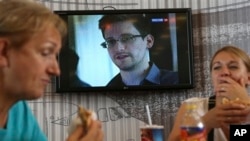 Para penumpang transit beristirahat di kafe bandara Sheremetyevo, Moskow, sementara layar TV menyiarkan berita Edward Snowden, Rabu (26/6).