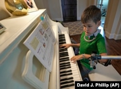 Braden Scott uses a device to support his left arm as he practices on the piano in Tomball, Texas on Friday, March 29, 2019. Braden was diagnosed with the syndrome called acute flaccid myelitis, or AFM, in 2016.