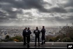 The city of Paris stretches out before French police officers as they stand guard near the church of Sacre Coeur, on top of the Montmartre hill, Nov. 18, 2015.