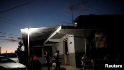 FILE - People gather to chat outside a mini-market that uses electricity from a generator, at the squatter community of Villa Hugo in Canovanas, Puerto Rico, December 12, 2017. 