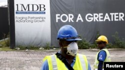 FILE - Construction workers stand in front of a 1Malaysia Development Berhad (1MDB) billboard at the Tun Razak Exchange development in Kuala Lumpur, Malaysia.