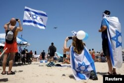 People watch a United Kingdom Royal Air Force Hercules fly over the Mediterranean Sea during an aerial show as part of the celebrations for Israel's Independence Day marking the 70th anniversary of the creation of the state, in Tel Aviv, Israel, April 19, 2018.