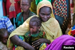 FILE - A mother and her child sit with other families at a camp for internally displaced people in Dougi, Cameroon, Oct. 24, 2013.