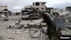 seorang laki-laki berjalan menuntun sepedanya di lokasi yang rusak, di desa yang berada ditangan pemberontak di Kota Douma, di timur Ghouta, dekat Damascus, Suriah, 30 Maret 2018.