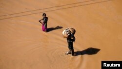 A girl stops to look as a man walks past carrying luggage on his head after Cyclone Idai in Buzi district outside Beira, Mozambique, March 22, 2019.