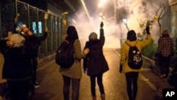 In this photograph taken Saturday, Jan. 11, 2020, protesters hold flowers as tear gas fired by police rises at a demonstration in front of Amir Kabir University in Tehran, Iran.