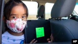 Second-grader Winona Begaye uploads homework in her family's vehicle in a dirt lot near Blue Gap, Ariz., on Sept. 25, 2020. (Megan Marples/Cronkite News via AP)