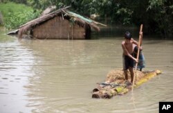 FILE - Flood-affected boys move on a banana raft near partially submerged houses in Morigaon district, east of Gauhati, Assam, India, Aug. 15, 2017.