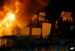 FILE - Protesters watch a fire on Sproul Plaza during a rally against the scheduled speaking appearance by Breitbart News editor Milo Yiannopoulos on the University of California at Berkeley campus, Feb. 1, 2017, in Berkeley, Calif.