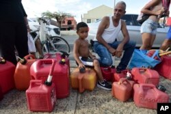 Ricardo Gonzalez sits on a gas container with his uncle Miguel Colon as hundreds of people wait in line since early morning hours to buy gasoline three days after the impact of Hurricane Maria in Carolina, Puerto Rico, Sept. 23, 2017.