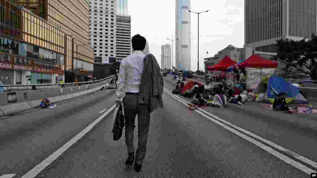 A man walks to work as the pro-democracy student protesters sleep on a roadside in the occupied areas surrounding the government complex in Hong Kong, Oct. 6, 2014. 