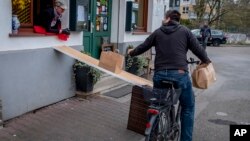 FILE - In this April 3, 2020, file photo, a man on a bike picks up food to go in front of the apple cider restaurant 'Zum Lahmen Esel' in Frankfurt, Germany. (AP Photo/Michael Probst, File)
