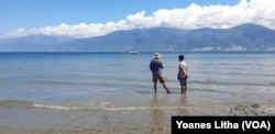 Dua orang warga mengamati perahu yang sedang membawa media transplantasi karang Jahe di pinggir pantai Mamboro, Palu Utara, Sulawesi Tengah, 21 Juli 2019. (Foto: VOA/Yoanes Litha)