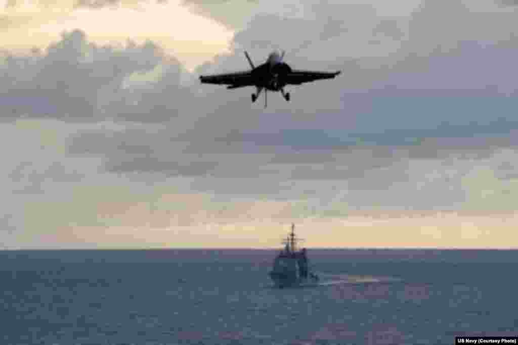 An F/A-18F Super Hornet from the Diamondbacks of Strike Fighter Squadron (VFA) 102, top, approaches to land on the flight deck of the aircraft carrier USS George Washington (CVN 73) while the Ticonderoga-class guided-missile cruiser USS Antietam (CG 54) t