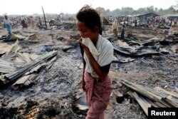 FILE - A woman walks among debris after fire destroyed shelters at a camp for internally displaced Rohingya Muslims in the western Rakhine state near Sittwe, Myanmar, May 3, 2016.