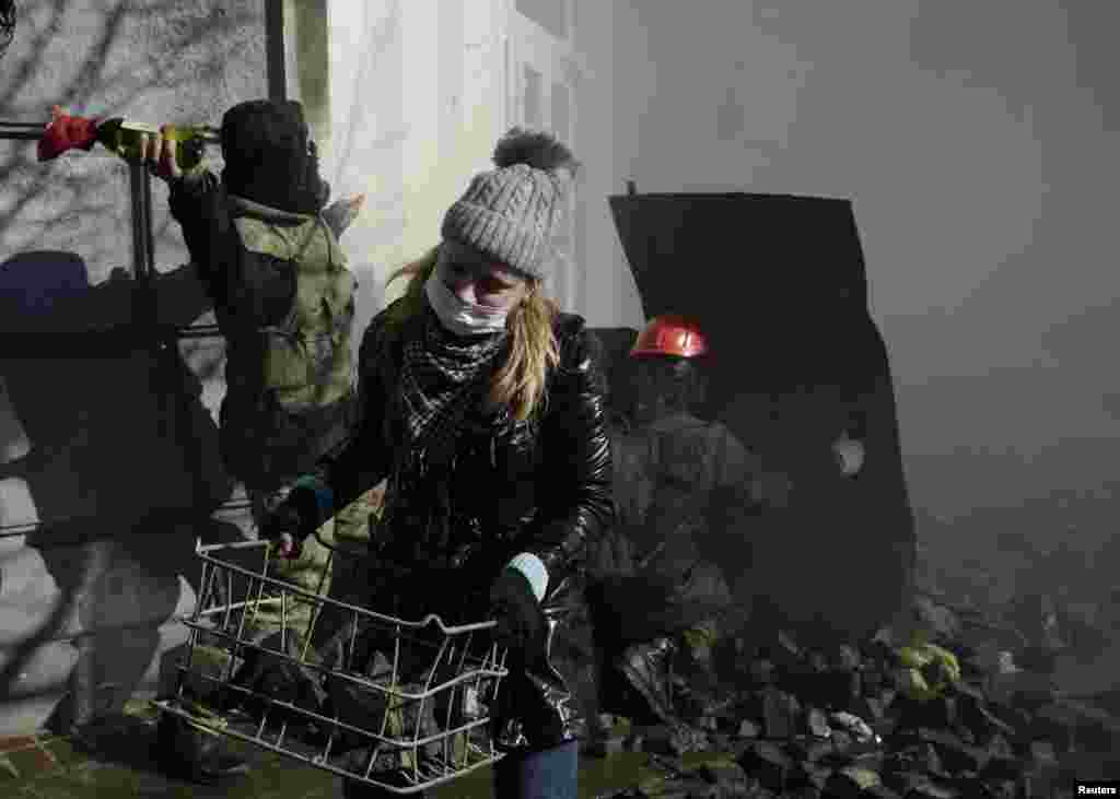 Seorang perempuan membawa batu dalam bentrokan antara demonstran anti-pemerintah dan para pegawai Kementerian Dalam Negeri di Kyiv (18/2).