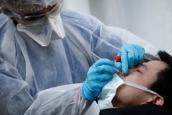 A medical biologist, wearing a protective suit, administers a nasal swab to a patient at a drive-through testing site for coronavirus disease (COVID-19) at the city hall of the 17th district in Paris