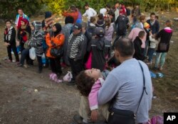 After crossing from Serbia into Asotthalom, Hungary, a man cradles a child and waits with other migrants for transfer to a refugee camp, Aug. 31, 2015.