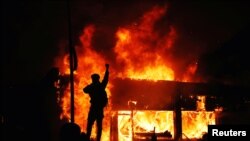 Seorang pengunjuk rasa di depan gedung yang terbakar di tengah demonstrasi yang terus berlanjut memprotes kematian George Floyd, pria Afrika-Amerika yang ditahan polisi, di Minneapolis, Minnesota, 30 Mei 2020.