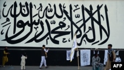 FILE - A vendor selling Taliban flags waits for customers next to a large Taliban flag in Kabul, Sept. 24, 2021.