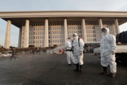 Workers wearing protective suits spray disinfectant as a precaution against the coronavirus at the National Assembly in Seoul, South Korea, Feb. 24, 2020.