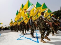 FILE - Iraqi Shi'ite Muslim men from the Iranian-backed group Kataib Hezbollah wave the party's flags as they walk along a street in Baghdad, July 25, 2014.