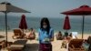 An employee of a beach bar, wearing a protective mask against the coronavirus, collects money for sunbed rentals, at Alimos beach, near Athens, Saturday, May 16, 2020. 