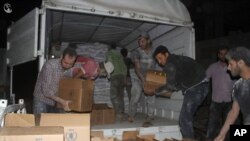 Warga Suriah mengeluarkan bantuan makanan dan bantuan lainnya dari truk Bulan Sabit Merah Suriah dan PBB di kota Daraya, pinggiran barat daya Damaskus, Jumat dini hari (10/6).