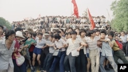 资料照片：1989年6月3日在北京人民大会堂附近，支持民主的抗议者手挽手阻止愤怒的人群追逐撤退的士兵。（美联社）