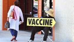 A seated man wearing a face mask holds a sign pointing to a mobile vaccination clinic on July 16, 2021, along Crenshaw Boulevard in Los Angeles, California. - Covid cases across America are rising in all 50 states as the Delta variant spreads with…