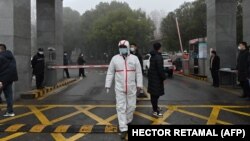 Seorang penjaga mengenakan APD terlihat di pintu masuk pusat pengendalian dan pencegahan penyakit provinsi Hubei saat anggota tim Organisasi Kesehatan Dunia (WHO) meninjau lokasi yang terletak di Wuhan, China, 1 Februari 2021. (Foto: HECTOR RETAMAL / AFP)