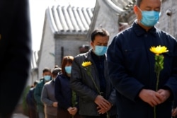 People holding flowers observe a moment of silence as China holds a national mourning for those who died of the coronavirus in Beijing, China, April 4, 2020. (cnsphoto via Reuters)