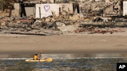 Kajakaš prolazi pored niza kuća oštećenih u požaru Palisades, 15. januara 2025. u Malibuu, Kalifornija.