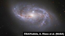 FILE - Looking deep into the Universe, the NASA/ESA Hubble Space Telescope catches a passing glimpse of the numerous arm-like structures that sweep around this barred spiral galaxy, known as NGC 2608. 