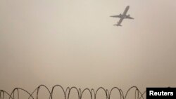 FILE - A plane flies in the polluted air above the airport fences in Beijing, Feb. 22, 2012.