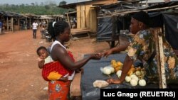 FILE - A woman buys fruit in the Ivorian cocoa farming village of Djigbadgi, commonly known as Bandikro or Bandit Town, located inside the Rapides Grah protected forest on January 7, 2021. (REUTERS/Luc Gnago)