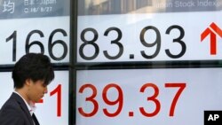 A man uses a mobile phone in front of an electronic stock indicator of a securities firm in Tokyo, Japan, Sept. 27, 2016. Asian stock markets were mostly higher as traders followed the U.S. presidential debate between candidates Hillary Clinton and Donald Trump. 