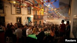 People sit outside in the Alfama neighborhood during the Festival of Popular Saints in Lisbon, Portugal, June 16, 2018.